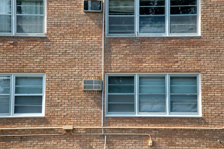 Ceglana ściana budynku z prostokątnymi oknami, żaluzjami, rurą pionową i dwiema klimatyzacjami