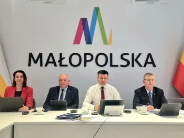 Cztery osoby siedzą przy stole konferencyjnym z laptopami i tabletami, na tle ściany z logo i napisem MAŁOPOLSKA.